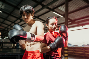 Female and male fighters stand in boxing gloves and pose back to back in the ring