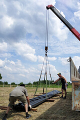 The workers support and direct the metal profile that unloads the truck crane.