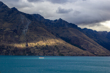 Obraz premium Ship on Lake Wakatipu on a cloudy day next to beautiful sun rays, Queenstown, New Zealand