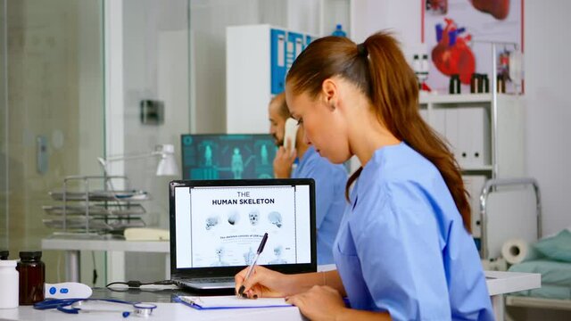 Doctor assistant analyzing digital human skeleton on laptop, taking notes on clipboard. Radiologist nurse in medicine uniform looking at digital radiography, bones examination, diagnosis