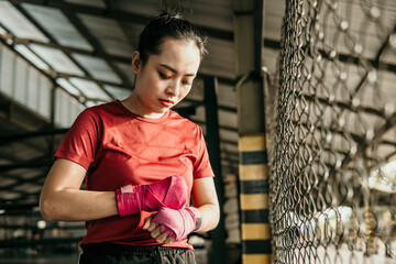 portrait of woman boxer fighter applying bondage tape on hands over fighting place background