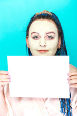 Jewish woman with blue afro braids face in a frozen mask of green clay holding a poster on a blue background.