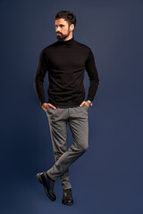 Naklejka premium Confident in his perfect look. Full length of confident young handsome man holding hands in pockets and looking side while standing against Pacific Blue background
