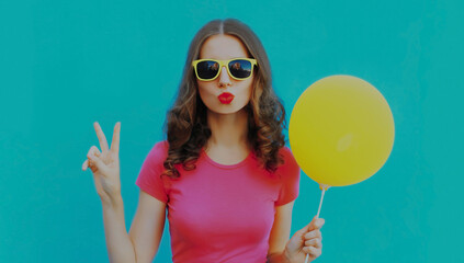 Summer portrait of young woman blowing her lips with yellow balloon on a blue background