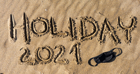 The inscription "Holiday" in the sand with the mask lying next to it.