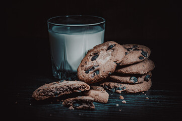 Stack of Chocolate chip cookies and glass of milk on dark wooden background with copy space.