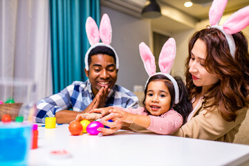 afro american man and caucasian woman ans their cute child painting eggs indoors
