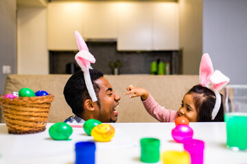 happy mixed race family celebrating Easter, painting eggs with brush smiling and laughing