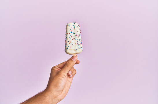 Hand Of Hispanic Man Holding Ice Cream Over Isolated Pink Background.