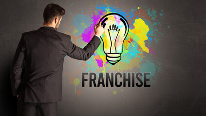 businessman drawing colorful light bulb with FRANCHISE inscription on textured concrete wall, new...