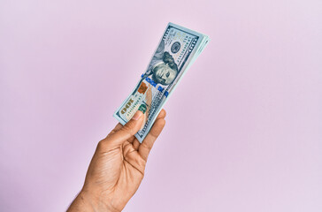 Hispanic hand holding usa dollars banknotes over isolated pink background.