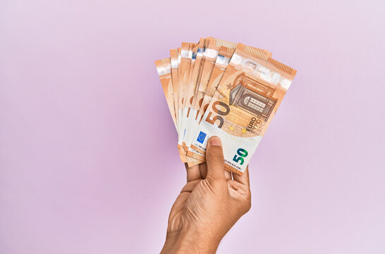 Hispanic hand holding 50 euro banknotes over isolated pink background.