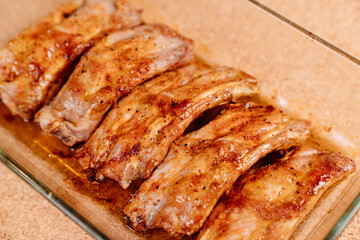 fried with spices pork ribs in a glass baking sheet on a wooden background. cooked meat at home. Barbecue.