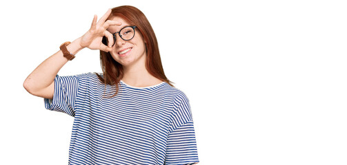 Young read head woman wearing casual clothes and glasses doing ok gesture with hand smiling, eye looking through fingers with happy face.