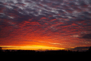 Beautiful Red Sunset In Cloudy Northern Germany With Windmills And Trees In The Background.