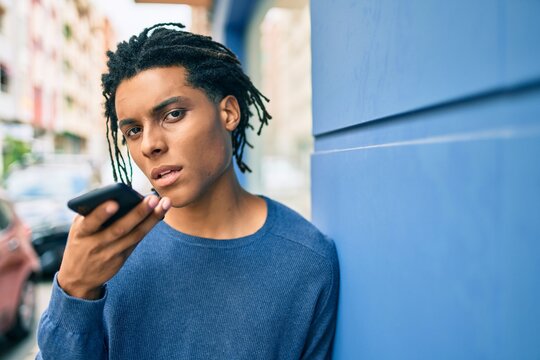 Young african american man with unhappy expression sending audio message using smartphone at street of city.