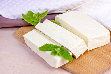 Raw organic vegetarian tofu slices with fresh mint on wooden background.