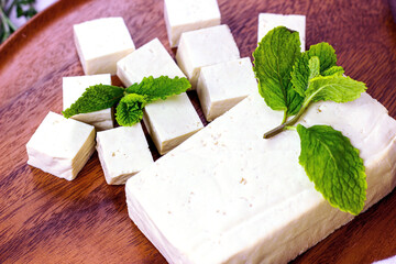 Raw organic vegetarian tofu slices with fresh mint on wooden background.