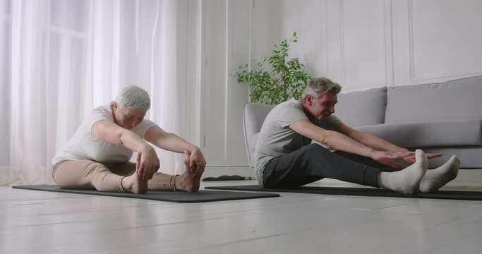 Senior couple doing physical stretching exercises together. Elderly man struggling to bend forward and touch toes. Endurance test.