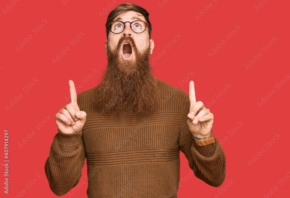 Wall mural young irish redhead man wearing casual clothes and glasses amazed and surprised looking up and point