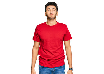 Fototapeta premium Young handsome man wearing casual red tshirt puffing cheeks with funny face. mouth inflated with air, crazy expression.