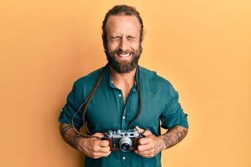 Handsome man with beard and long hair holding vintage camera smiling and laughing hard out loud...