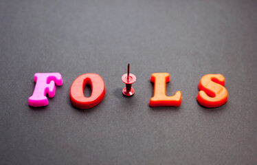 The word fools from color letters with a pushpin on a black background. April Fools' Day, April 1, not trusting anyone, jokes.