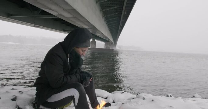 Man In Winter Coat Sitting Next To The Bonfire Under The Ruoholahden Silta. - close up