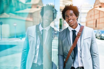 Fototapeta premium Young handsome african american businessman wearing suit smiling happy. Leaning on the wall with smile on face at town street.