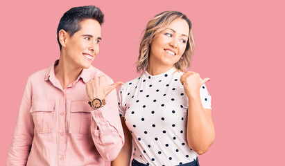 Couple of women wearing casual clothes smiling with happy face looking and pointing to the side with thumb up.