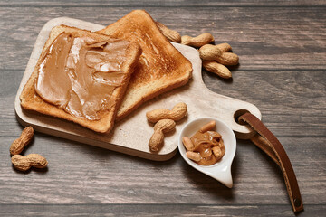 Creamy peanut butter breakfast toast on a wooden cutting board with fresh peanuts.