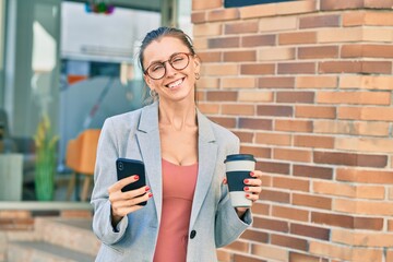 Young blonde businesswoman using smartphone and drinking coffee at the city.