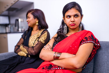 two young indian women in traditional sari and bindi looking in different sides in interior of living room