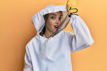 Beautiful blonde caucasian woman wearing protective beekeeper uniform surprised with hand on head for mistake, remember error. forgot, bad memory concept.