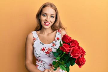 Beautiful blonde caucasian woman holding bouquet of red roses looking positive and happy standing and smiling with a confident smile showing teeth