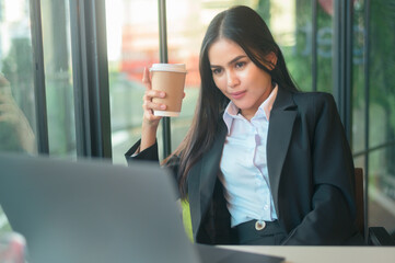 A beautiful business woman is analyzing financial data via computer , drinking coffee in coffee shop . business people lifestyle . technology concept ...