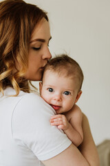 Beautiful mom hugs and kisses the newborn in the studio on a white background. A young mother in a white bodysuit hugs and kisses her newborn daughter in the studio.