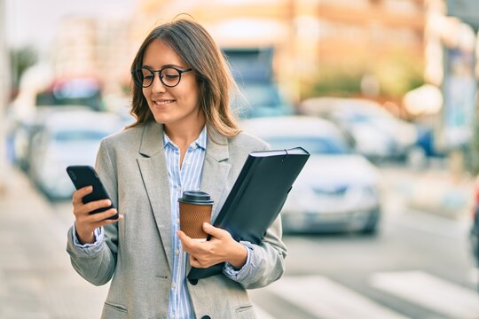Young hispanic businesswoman using smartphone and drinking take away coffee at the city.