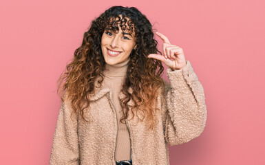 Young hispanic girl wearing winter clothes smiling and confident gesturing with hand doing small size sign with fingers looking and the camera. measure concept.