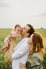Young parents hug and kiss their newborn daughter in nature.