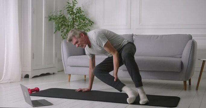 Elderly gray-haired man unable to stand up from yoga mat because of knee joint sharp pain.