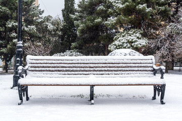 Bench in city park is covered with snow