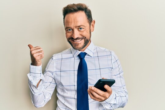 Middle age businessman using smartphone smiling happy pointing with hand and finger to the side