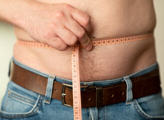 Closeup of measuring a male belly with a tailor's meter. The man shows his naked belly © Maria Rzeszotarska