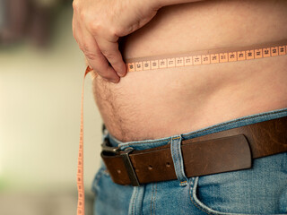Closeup of measuring a male belly with a tailor's meter. The man shows his naked belly