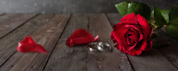 Wedding rings and red roses on wodden  vintage background. Horizontal romantic still life for a wedding concept. 