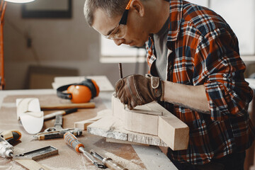 Craftsman cutting a wooden plank. Worker with wood. Man in a cell shirt.