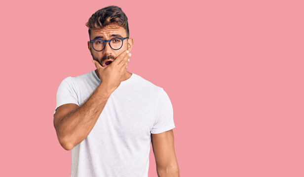 Young hispanic man wearing casual clothes and glasses looking fascinated with disbelief, surprise and amazed expression with hands on chin