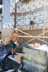 The master throws a brick at his worker for laying the wall.