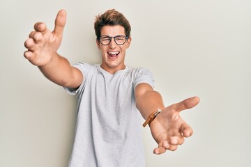 Handsome caucasian man wearing casual clothes and glasses looking at the camera smiling with open arms for hug. cheerful expression embracing happiness. © Krakenimages.com
